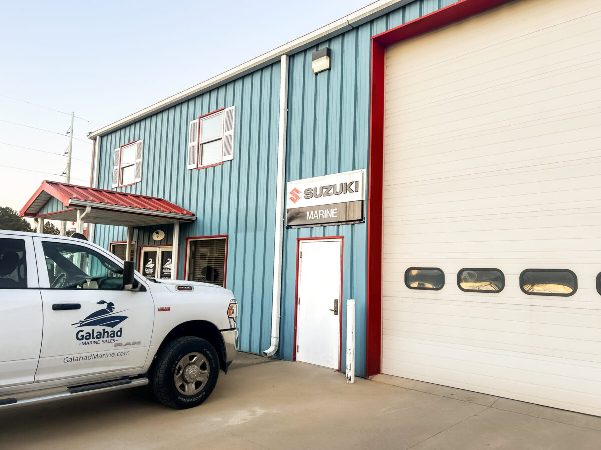 Blue metal-sided marine service building with a white Suzuki Marine sign, large garage door, and a Galahad Marine Sales truck parked out front.