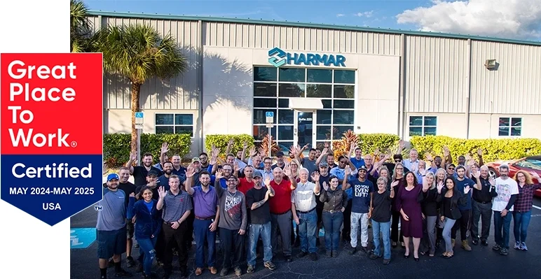 A large group of people in front of a building with a "Harmar" sign, standing next to a "Great Place to Work Certified" emblem, dated May 2024-May 2025.