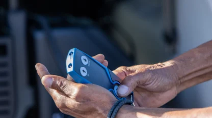 Hands holding a blue remote control device with two buttons, possibly operating machinery or equipment.