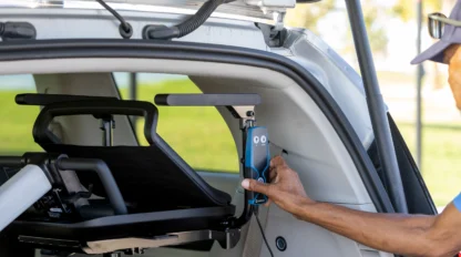 A person operates a mechanical lift to load a wheelchair into the back of a vehicle. The lift is attached inside the car.
