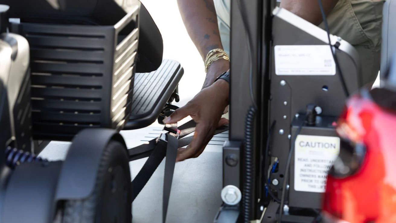 Person securing a mobility scooter with straps in a vehicle.