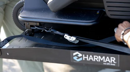 A person secures a mobility device onto a Harmar vehicle lift using a strap and buckle.