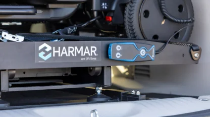 Close-up of a Harmar wheelchair lift installed in a vehicle, with a blue control panel featuring buttons attached to the lift platform.
