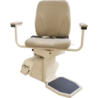 A beige stair lift chair with padded seat, armrests, and a footrest, mounted on a motorized platform.