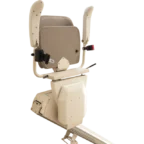 A beige stairlift seat with armrests and safety belt, mounted on a rail system, positioned against a neutral background.