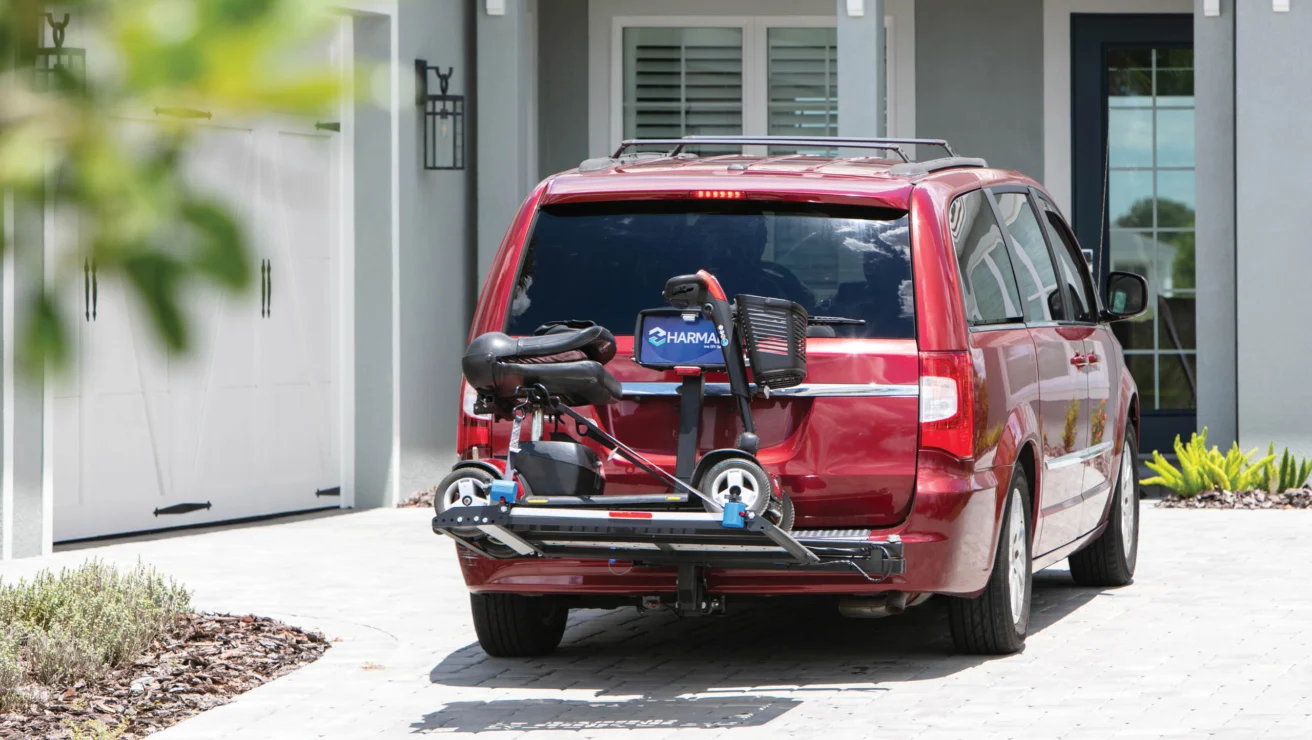 A red minivan parked in a driveway with a mobility scooter attached to its rear on a carrier.