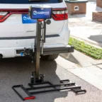 Vehicle-mounted wheelchair lift attached to the back of a white SUV parked on a street.