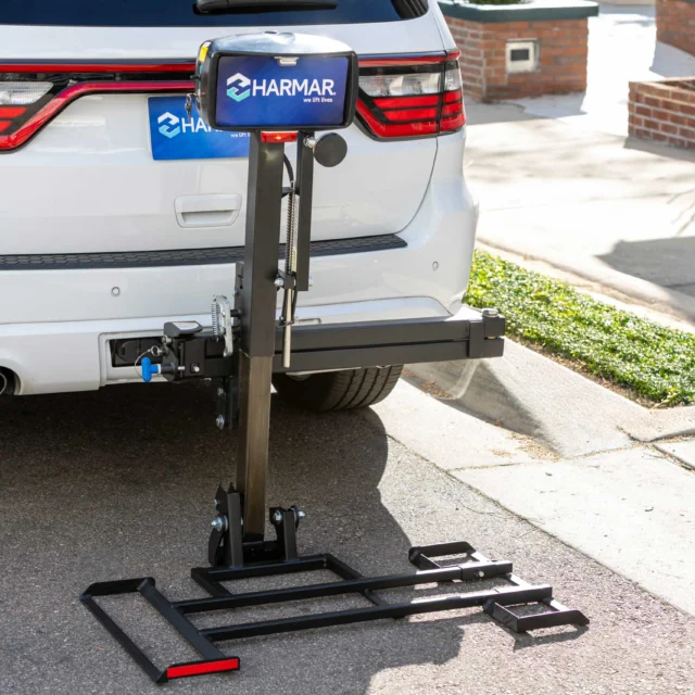 Vehicle-mounted wheelchair lift attached to the back of a white SUV parked on a street.