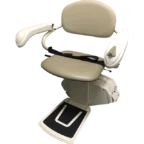 A beige stairlift chair with armrests, seatbelt, and footrest, designed for assisting individuals in moving up and down stairs.