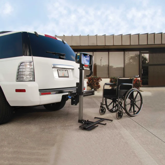 A wheelchair lift attached to the rear of a white SUV near a building on a clear day.