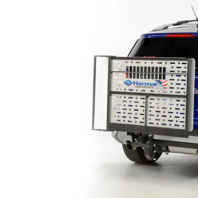 Blue SUV with a Harmar AL301XL lift attached to the rear, featuring a metallic platform for mobility devices, against a white background.