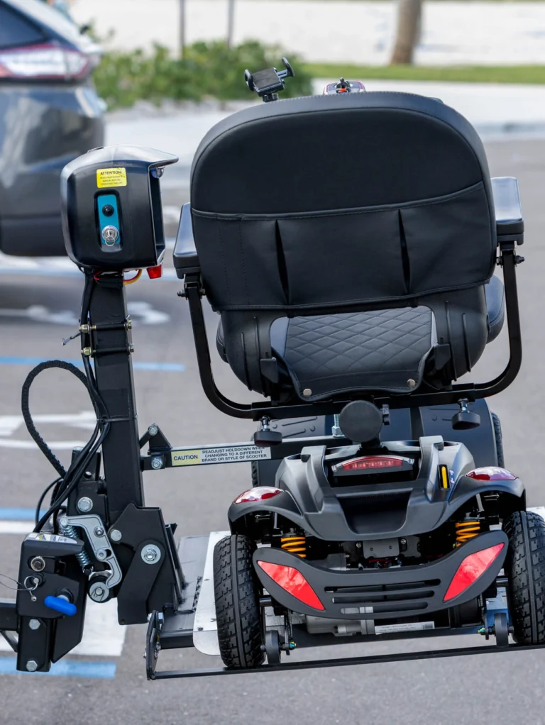 A mobility scooter is mounted on a carrier attached to the back of a white vehicle in a parking lot.