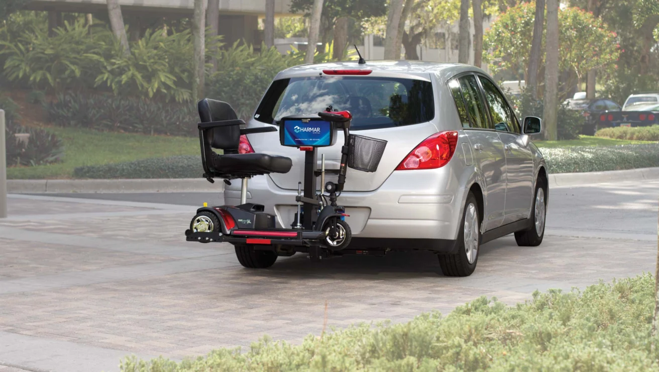 A car parked on a paved area with a mobility scooter attached to a rear-mounted carrier.