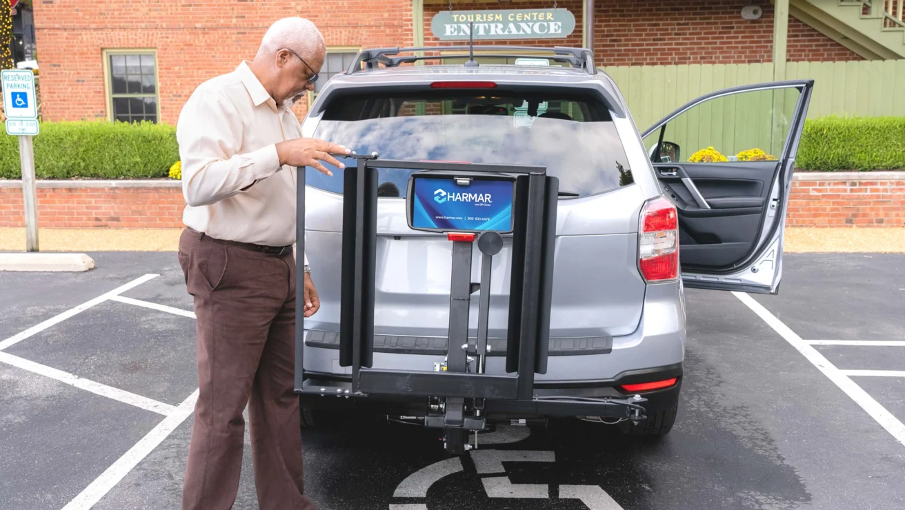 Man securing a mobility scooter lift to the back of a parked SUV in a designated accessible parking space.