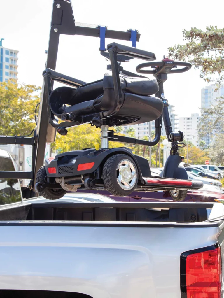 Motorized scooter mounted on a lift attached to a white pickup truck in a parking lot, with buildings and trees in the background.