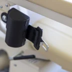 Close-up of a black seat belt buckle on a tan seat, with stitching detail and a lever visible.