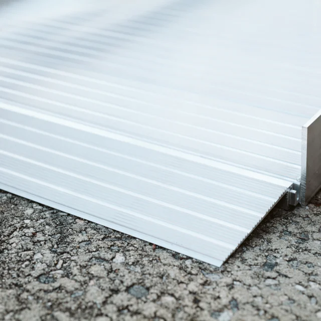 Close-up of a metal ramp transitioning from a concrete surface, showing screws and an aluminum frame.