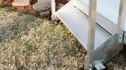 Metal step with railing leading from a platform onto a grassy area with stepping stones nearby.