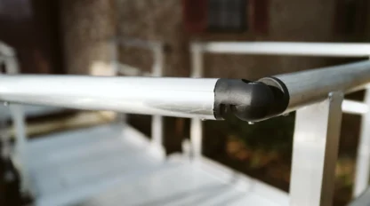 Close-up of a metal railing corner with a black connector, against a blurred background of a building facade.
