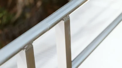 Close-up of a metal handrail with sunlight reflecting on its surface. The background is blurred.
