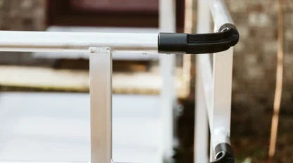 Close-up of a metallic handrail with black plastic end caps on an outdoor staircase.
