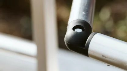 Close-up of a metal railing featuring a corner joint. The rails are silver with black connectors, partially blurred background.