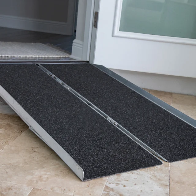 A portable ramp with a textured surface is placed at an open doorway, leading from an interior tiled floor to an exterior space.