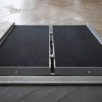 Foldable wheelchair ramp placed at an entrance on tile flooring, featuring a non-slip surface and metallic edges.
