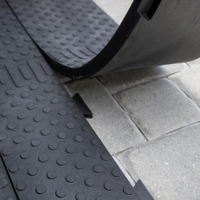 Rubber matting being installed on a paved surface, showing interlocking edges and textured grip pattern.
