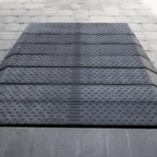 A black rubber cable protector with multiple channels is laid on a stone-paved surface.