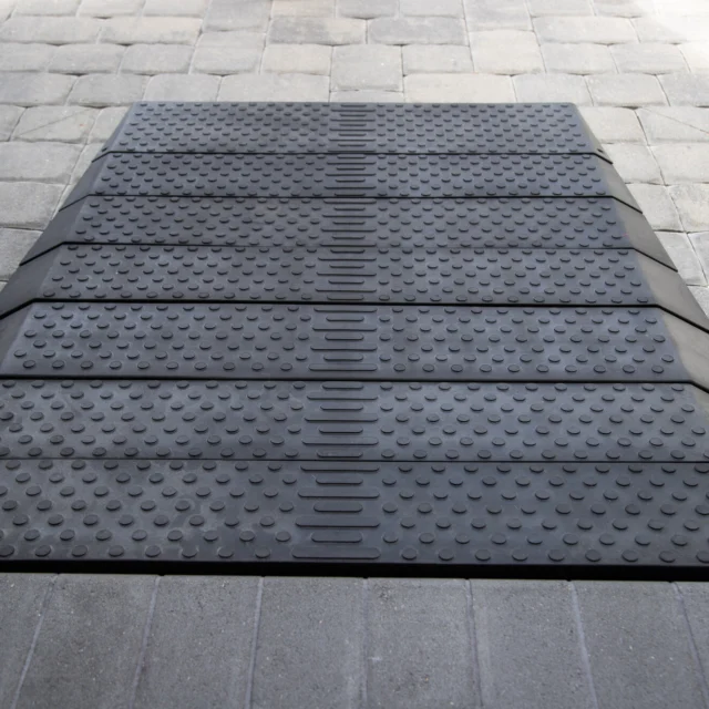 A black rubber cable protector with multiple channels is laid on a stone-paved surface.