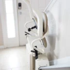 A stairlift installed along a staircase in a home, with folded seat and armrests, near a doorway with natural light.