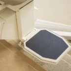 Close-up of a stairlift seat positioned at the top of a carpeted staircase, showcasing the safety grip surface.