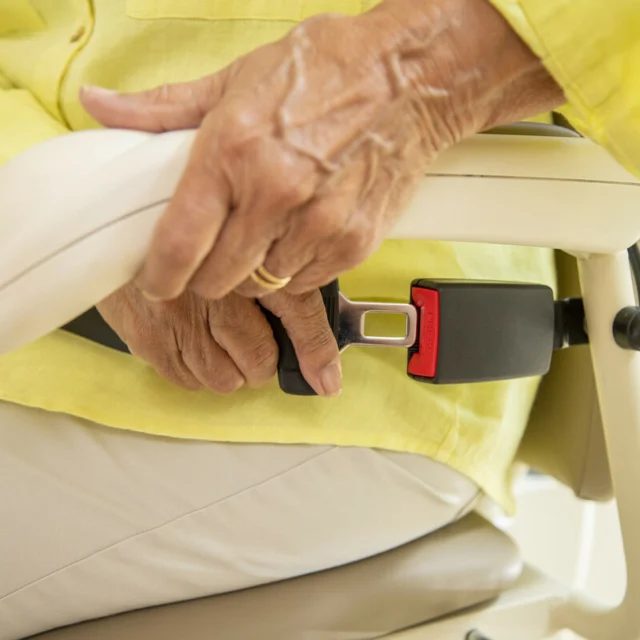 A person in a yellow shirt fastens a seatbelt on a stairlift chair.