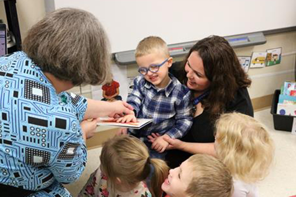 Children captivated by woman's 3D pen book art.