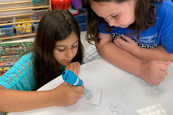 Girls using 3D pen for table drawings