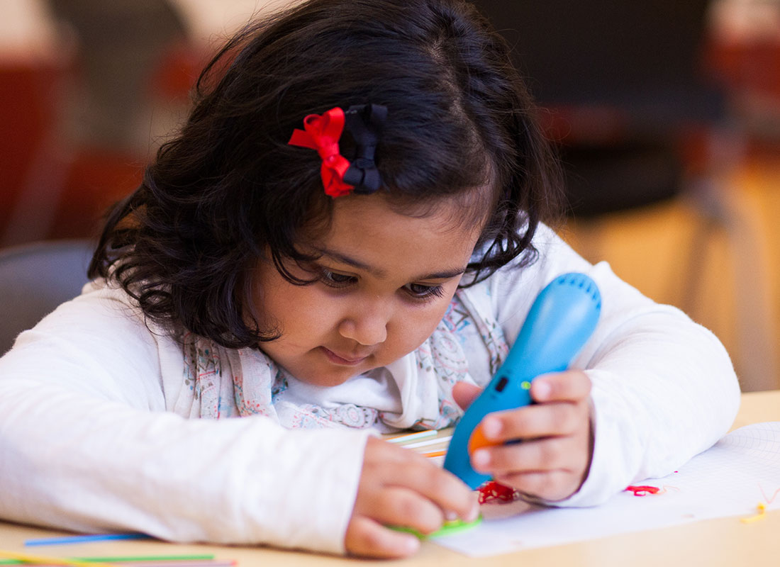 Young girl creatively using a 3D pen on paper.