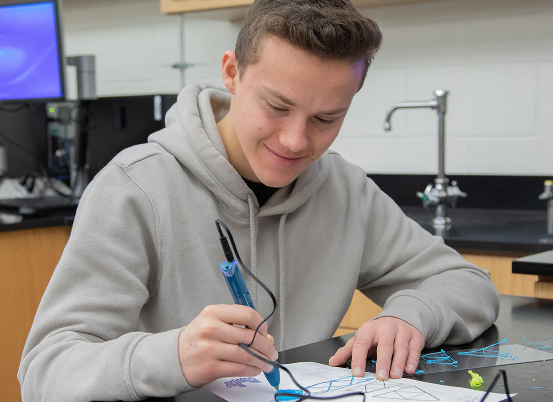 Male in grey sweatshirt creating 3D pen art.