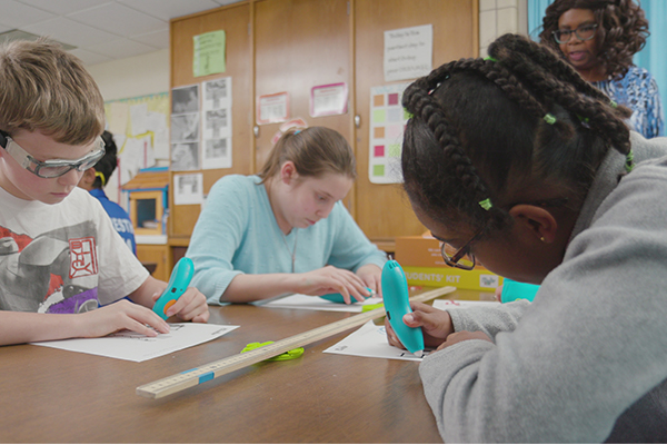 Children creating 3D pen art at table with ruler and paper.