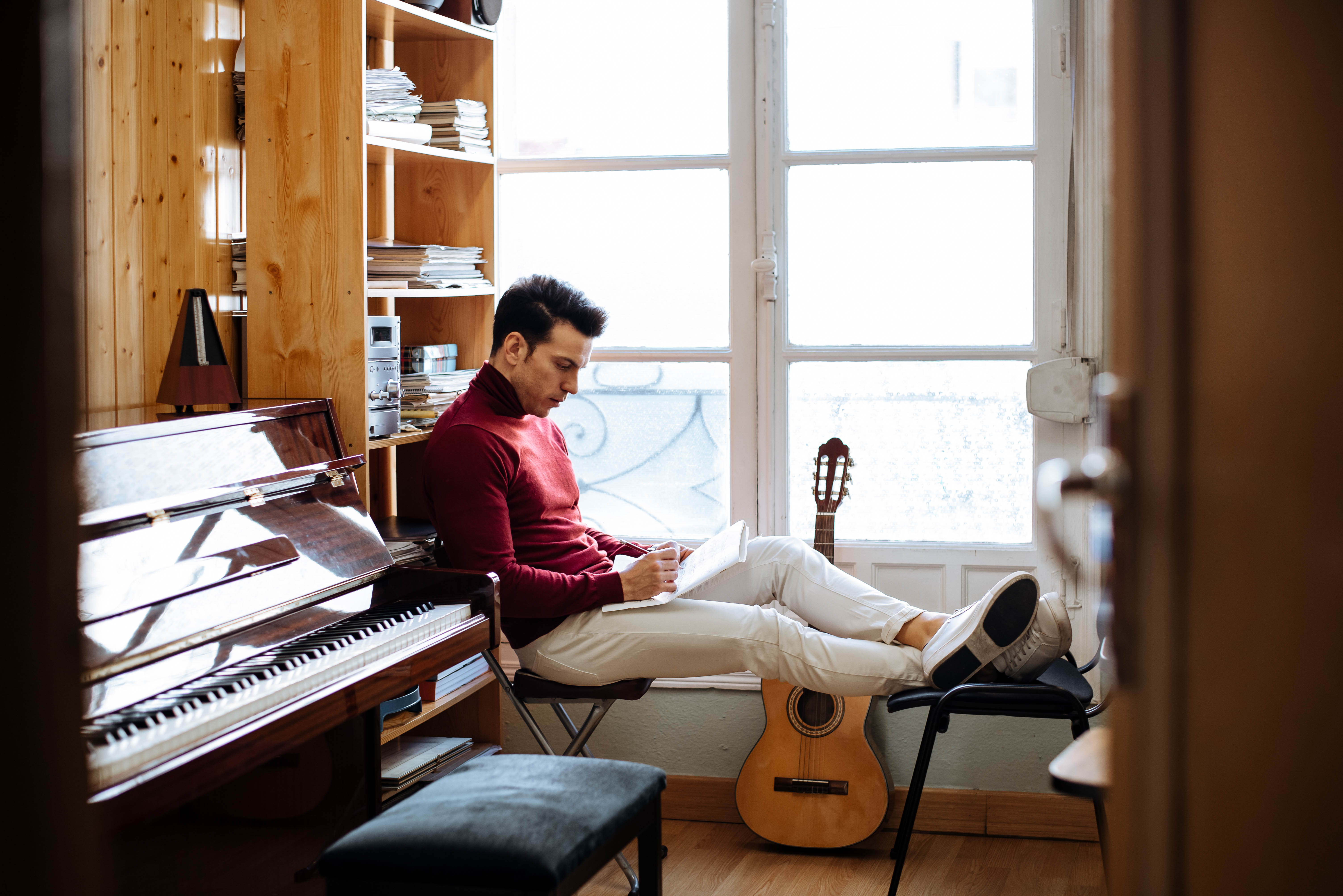 Male songwriter sitting by a window composing music in a notebook