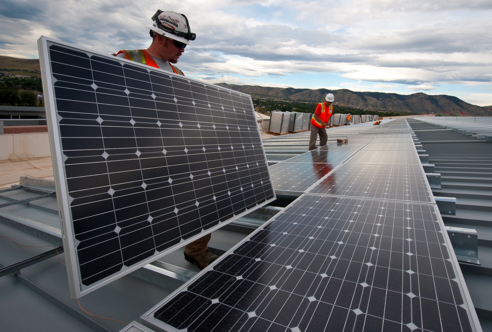 man in red shirt and black pants standing near solar panels during daytime