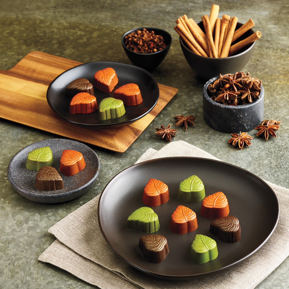 Orange, brown and green chocolate leaves featured next to cloves, cinnamon, and star anise