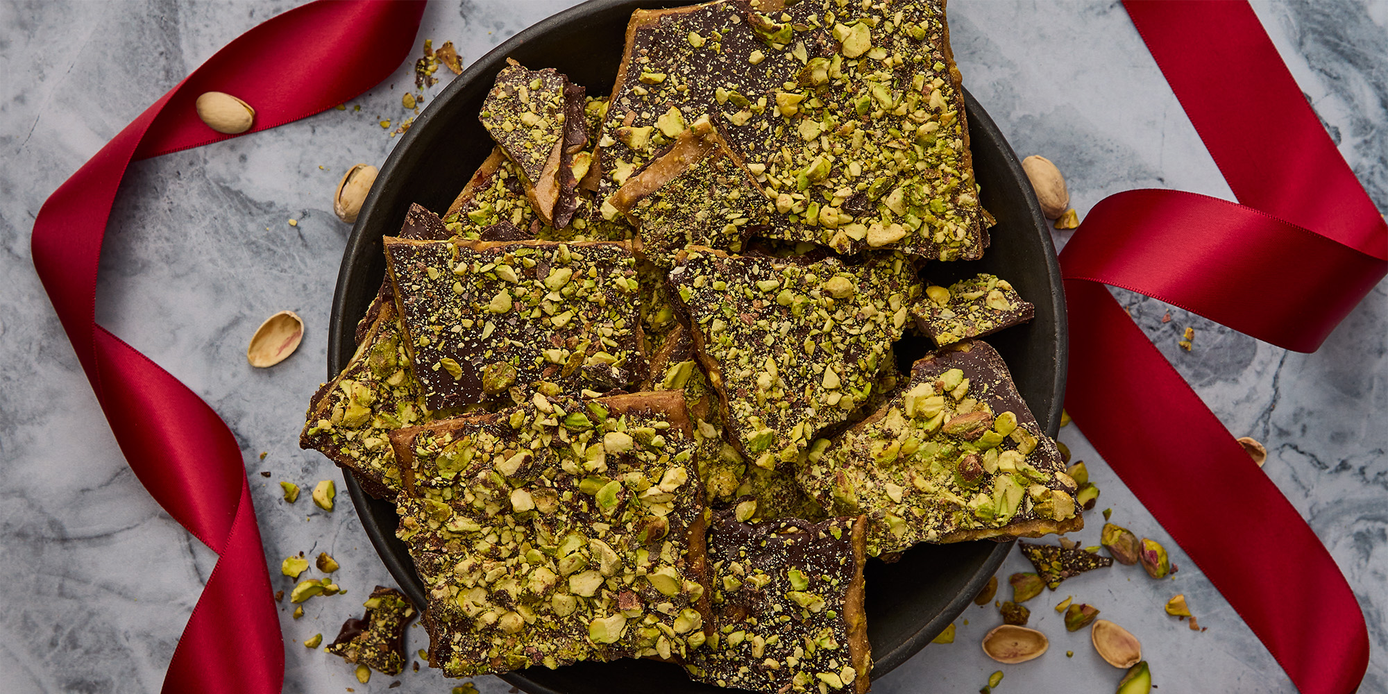 Pieces of buttery toffee topped with toasted bright green pistachios on a layer of rich dark chocolate
