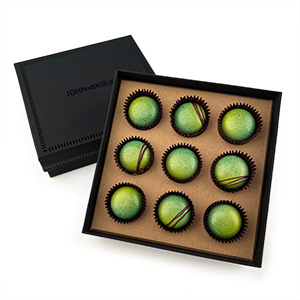 An open box of bright green chocolate bon bons that shows the black exterior of the package.