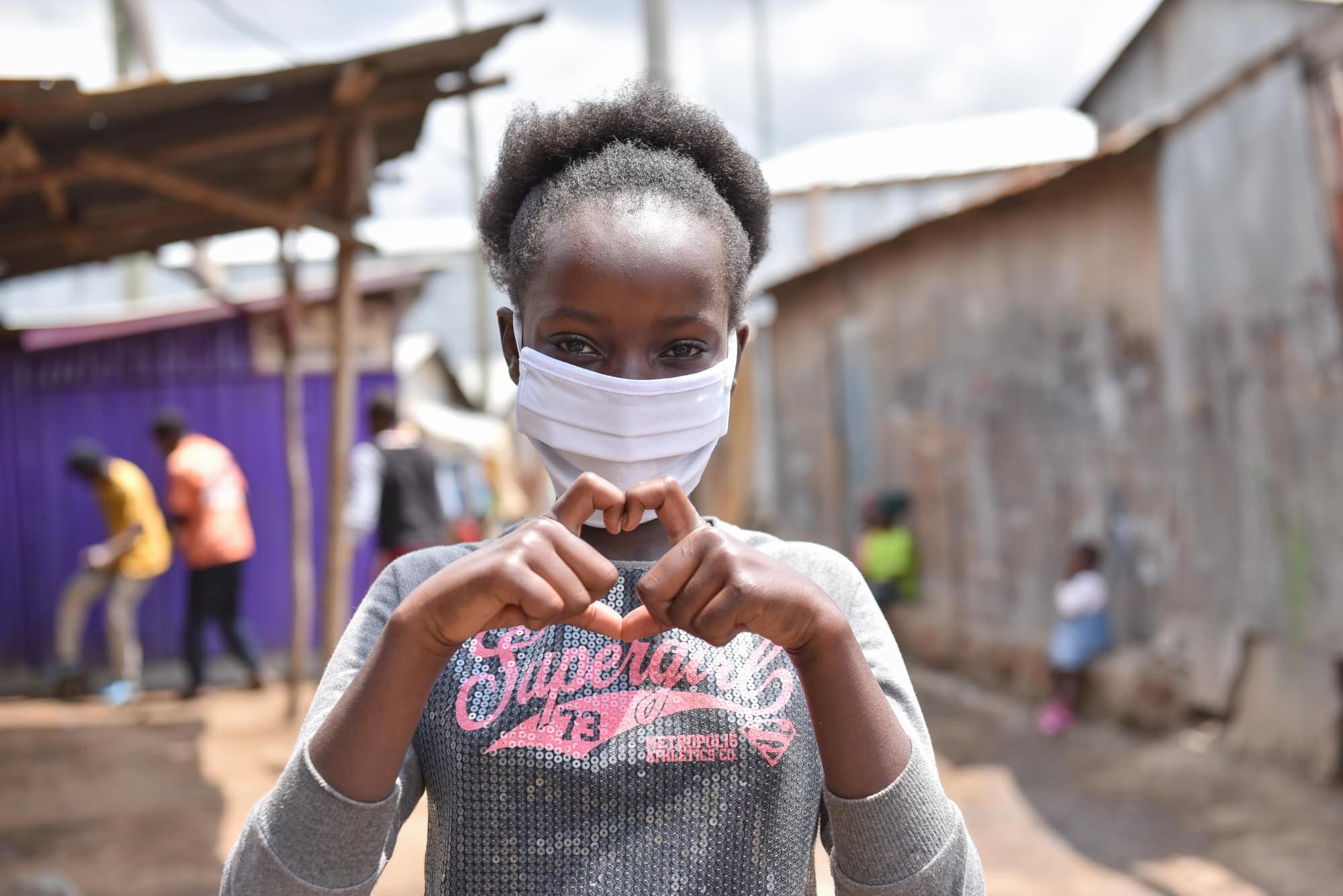 A young girl wearing a mask and making a heart with her hands