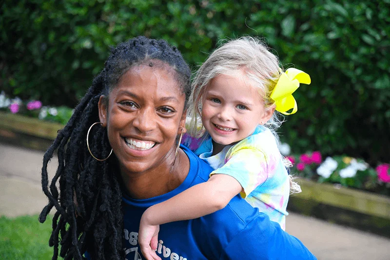 A staff member giving a young camper a piggy back ride.