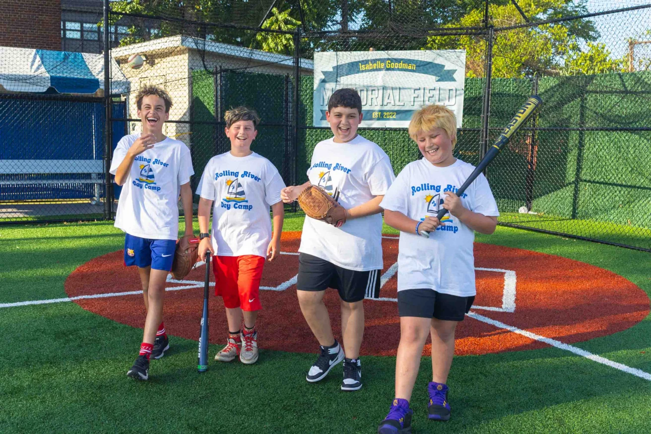 Four children in matching "Rolling River Day Camp" shirts stand on a baseball field, smiling and holding baseball equipment.