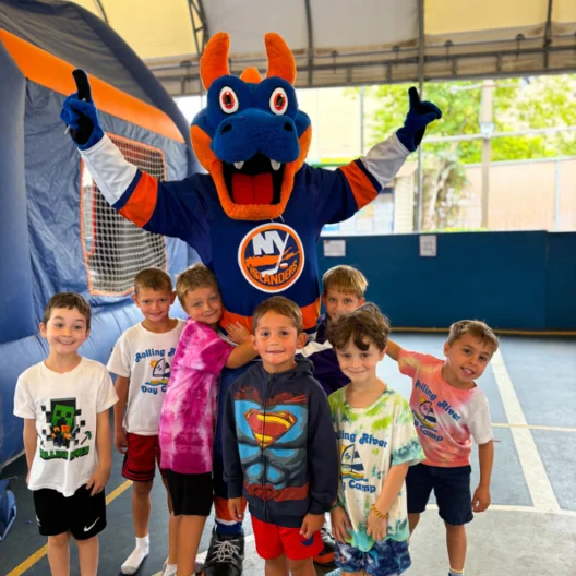 A group of children pose in front of an inflatable play area with a person dressed as an Islanders mascot, wearing a blue and orange costume.