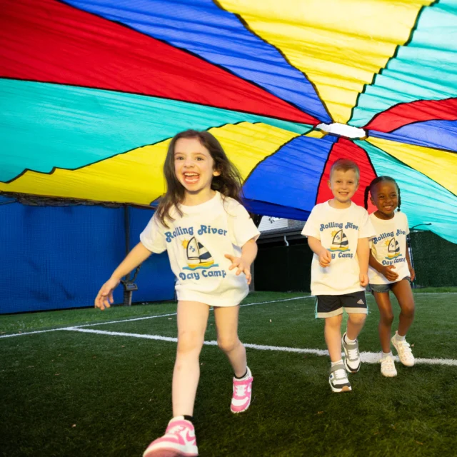 A group of campers playing underneath a rainbow tarp.