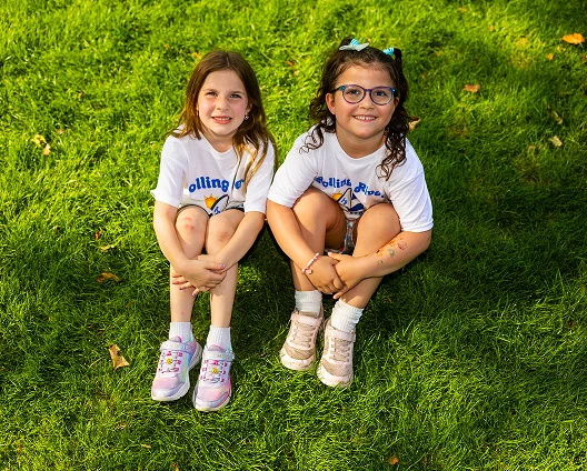 Two campers sitting on the grass, smiling.